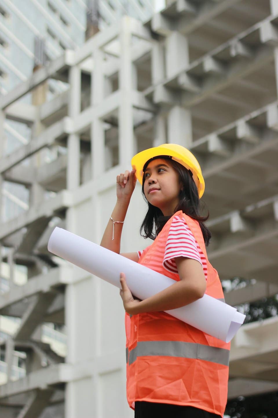 Donna con casco e giubbotto di sicurezza con progetti in cantiere.