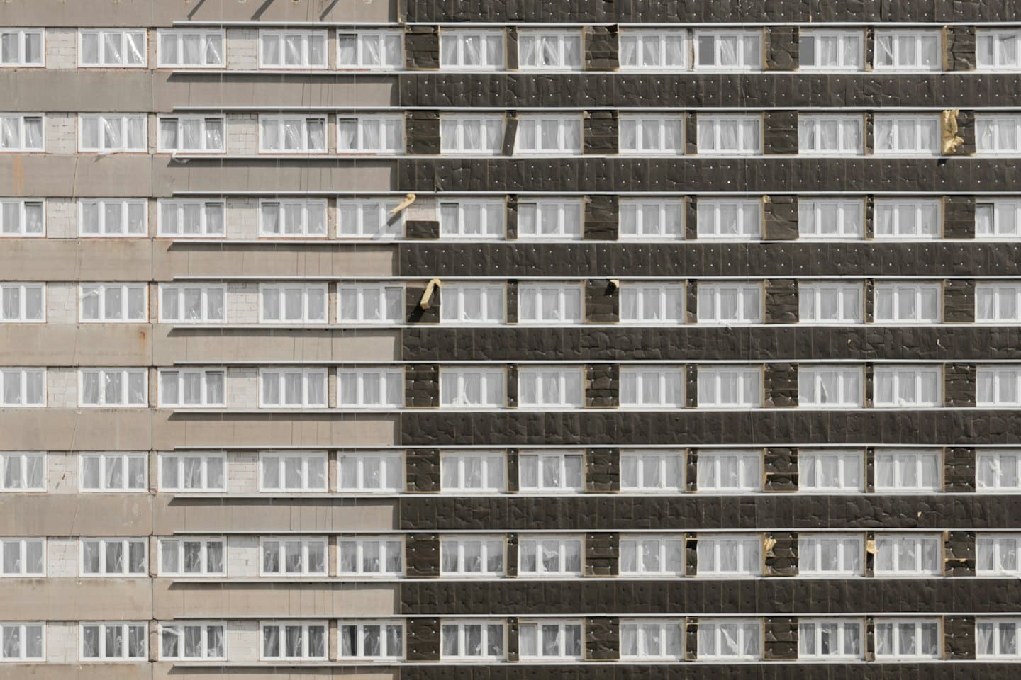 Facciata di un edificio divisa tra vecchio cemento e nuovi pannelli isolanti.